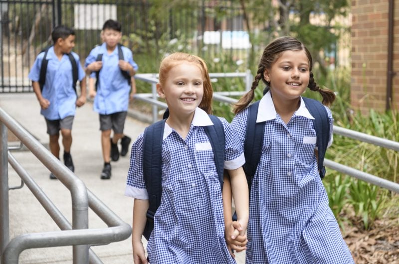 Female primary school students wearing blue gingham dresses with boys in background