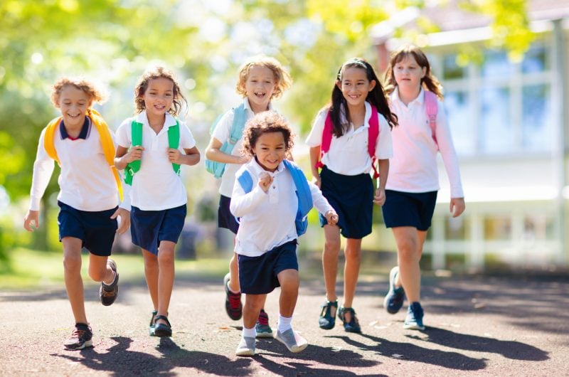 Kids go back to school. Interracial group of children of mixed age run and cheer on the first day of new academic year. Start of school holiday. Preschooler or kindergarten kid. Child in school yard.
